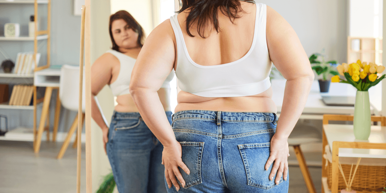 Young woman looking at herself in the mirror, conflicted about her appearance.
