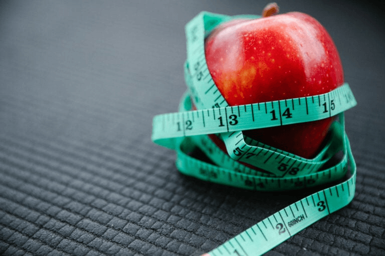 An image of an apple with a tape measure wrapped around it.