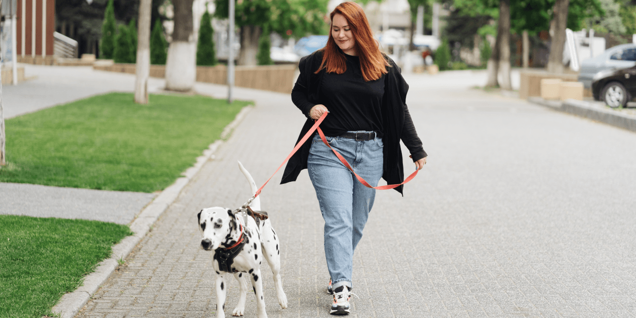 A young woman walking her Dalmatian dog in a neighbourhood, surrounded by greenery.