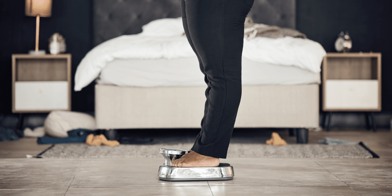 Woman weighing herself in her bedroom using a metal scales