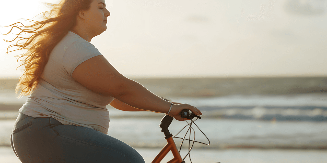 Young woman cycling at sunset alongside the sea. She looks happy and fulfilled.