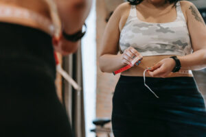 woman measuring her waist with tape measure in front of a mirror